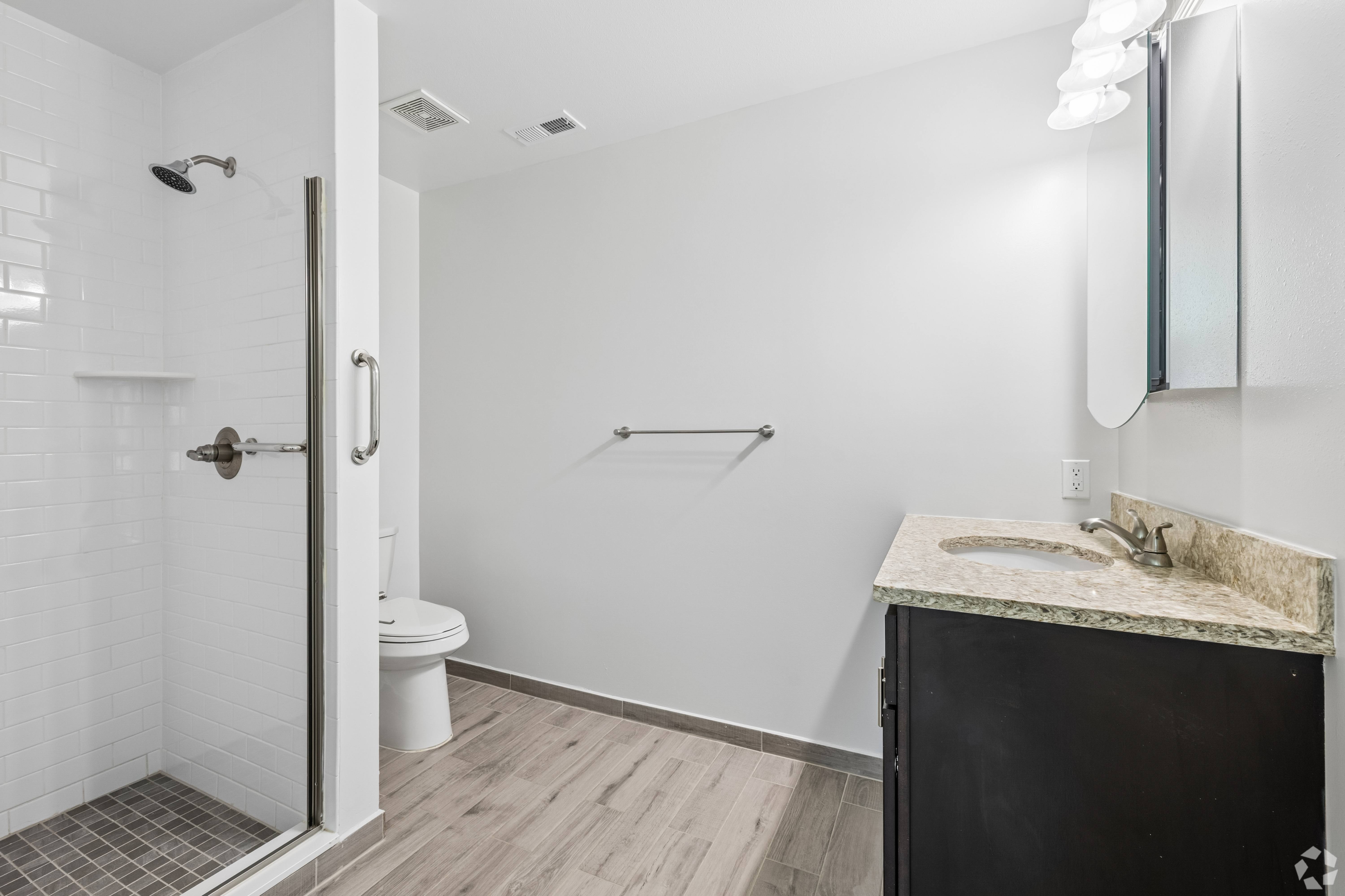 A bathroom with a white tile shower and a black vanity.